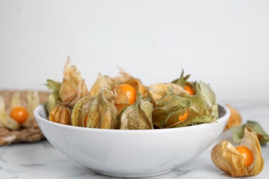 Ripe physalis fruits with dry husk on white marble table