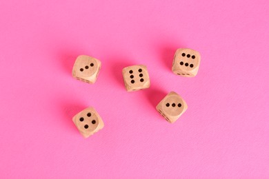 Many wooden game dices on pink background, flat lay