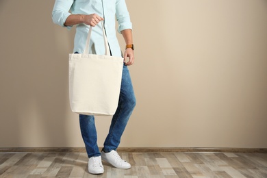Photo of Young man holding textile bag against color wall, closeup. Mockup for design