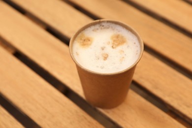 Takeaway paper cup with coffee on wooden table, closeup