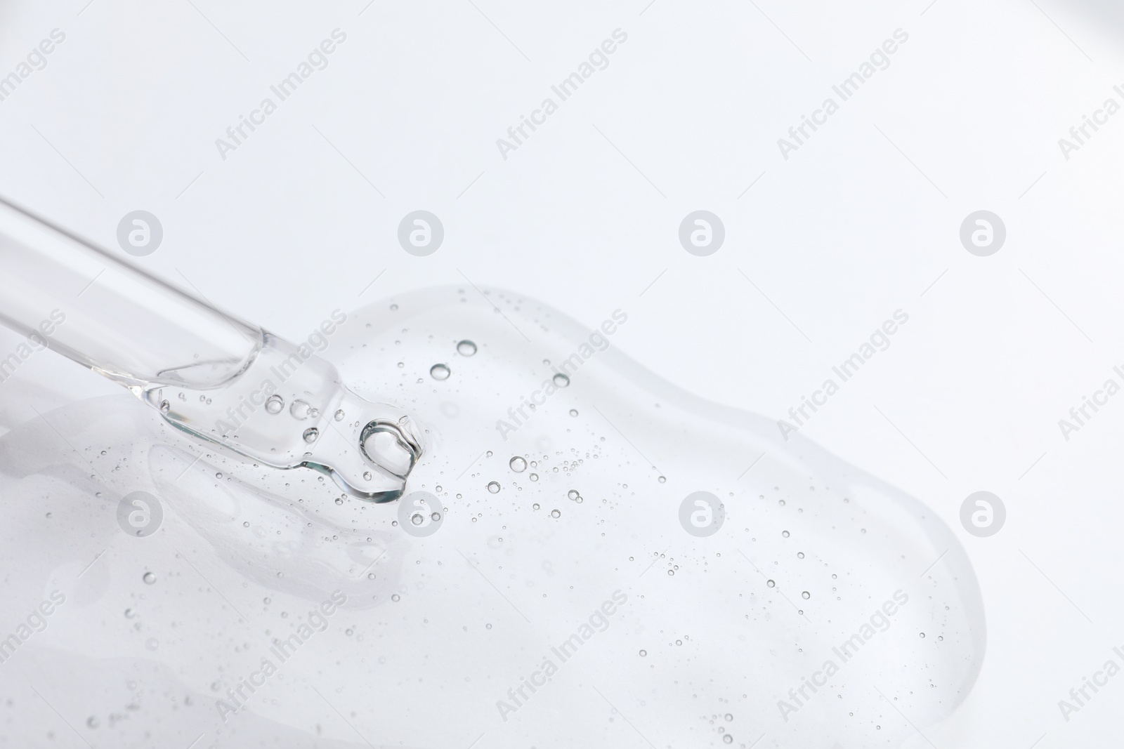 Photo of Dripping cosmetic oil from pipette onto light surface, closeup. Space for text
