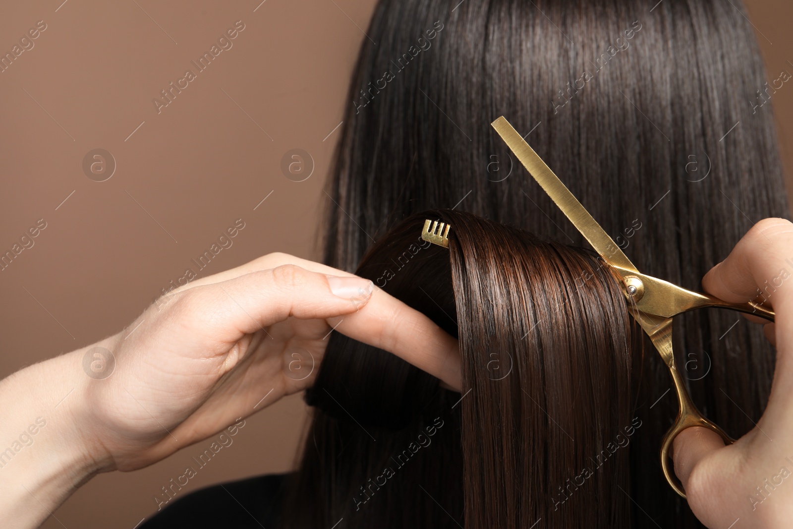 Photo of Hairdresser cutting client's hair with scissors on light brown background, closeup