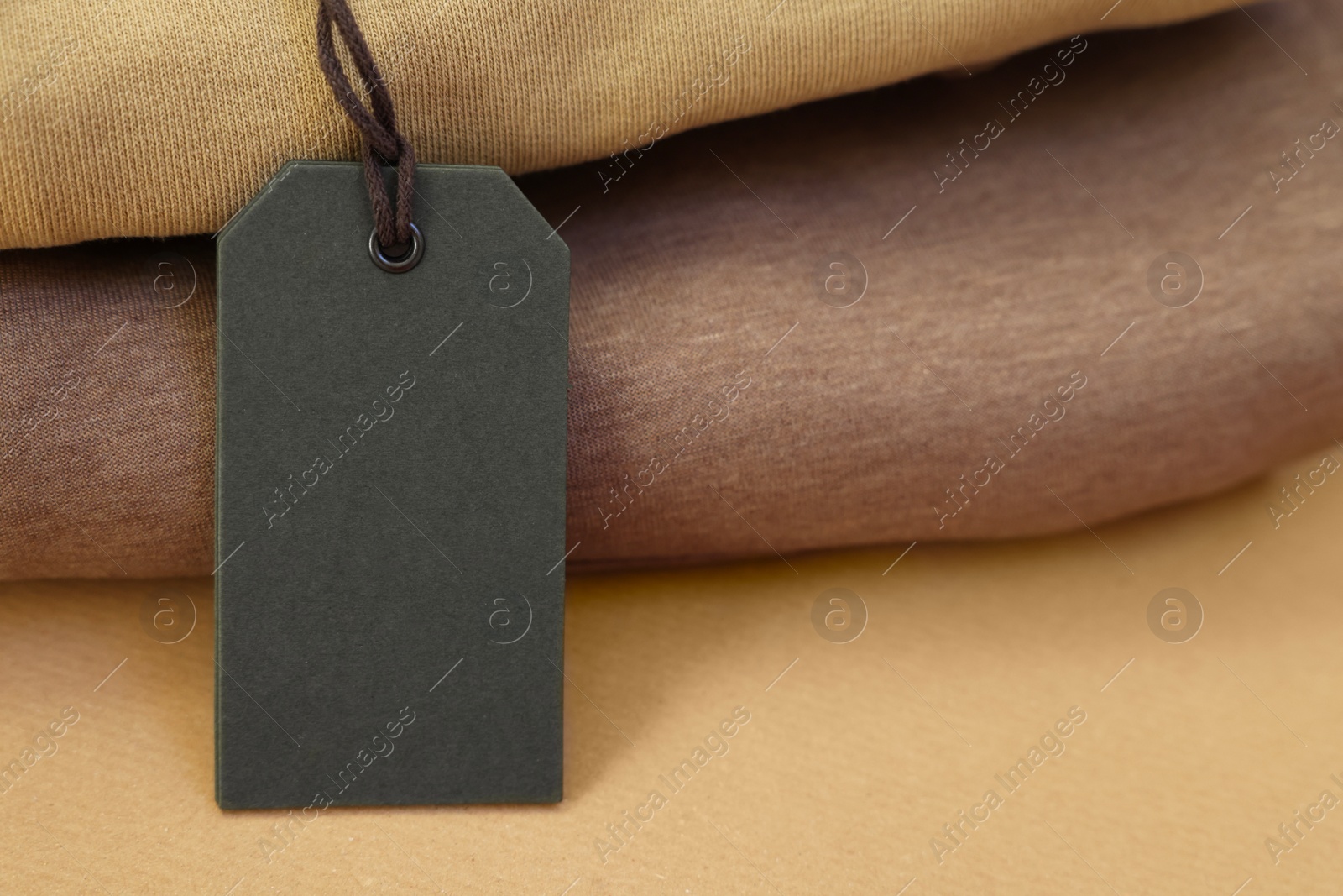 Photo of Garment with cardboard tag on kraft paper sheet, closeup. Space for text