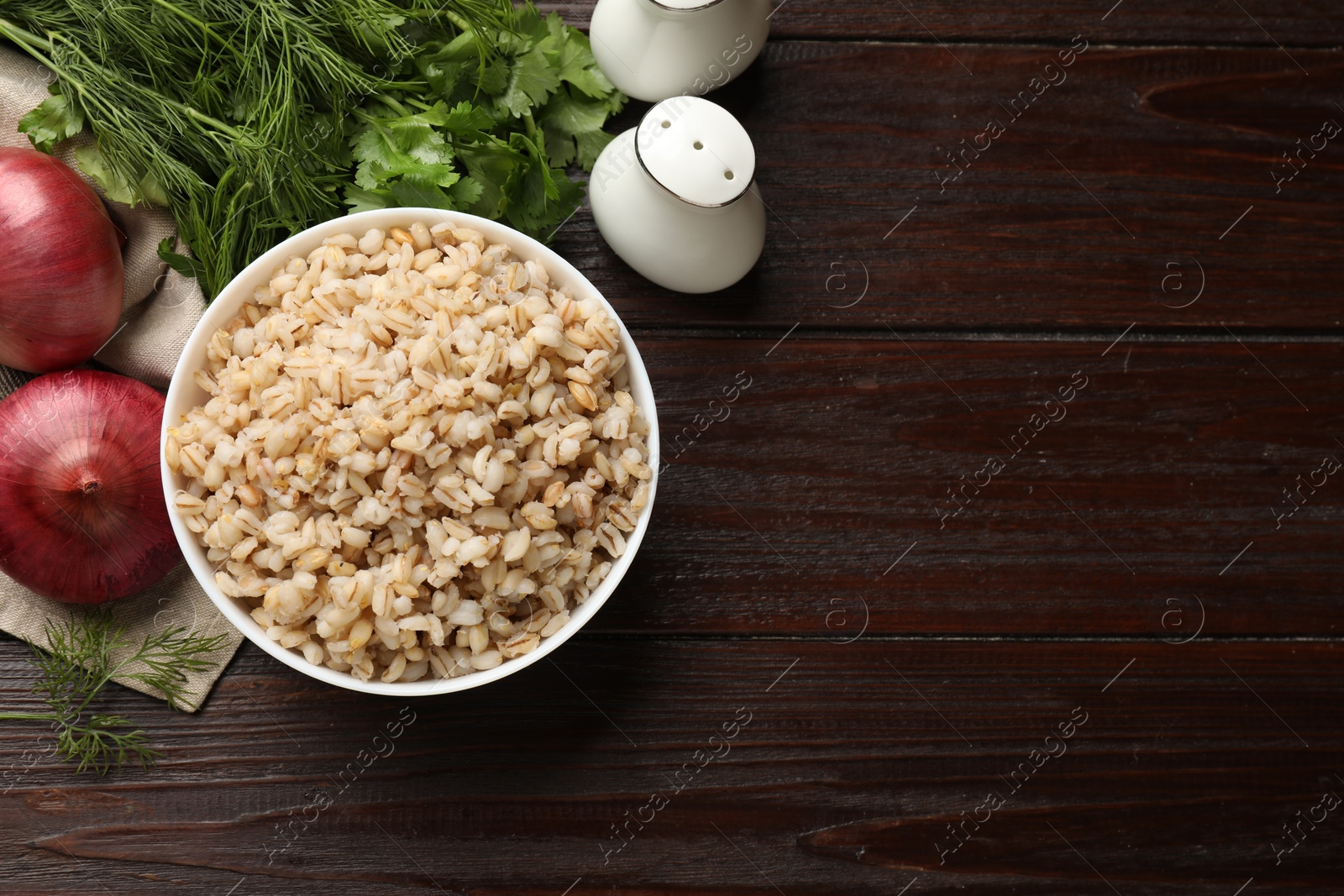 Photo of Delicious pearl barley in bowl served on wooden table, top view. Space for text