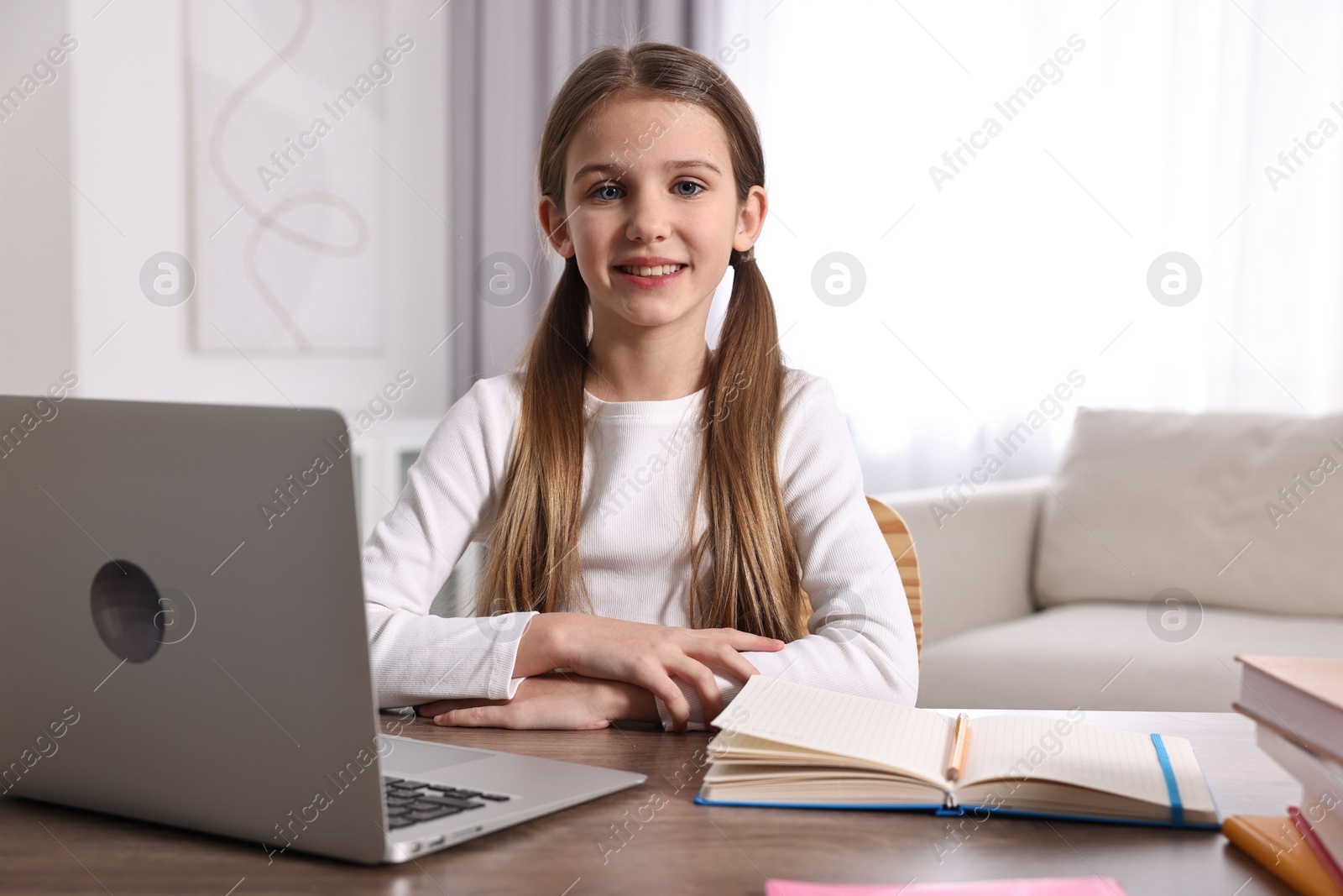 Photo of E-learning. Cute girl using laptop during online lesson at table indoors