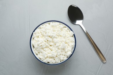 Photo of Delicious fresh cottage cheese in bowl near spoon on grey table, flat lay