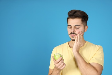 Young man with sensitive teeth and apple on color background. Space for text