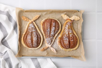 Photo of Delicious pears baked in puff pastry with powdered sugar on white tiled table, top view