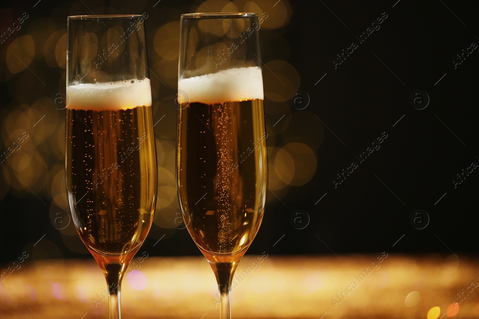 Photo of Glasses of champagne with golden bubbles on blurred background. Space for text
