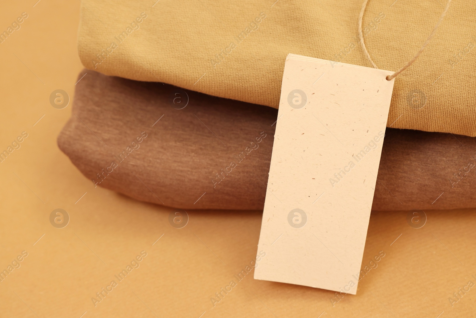 Photo of Garment with cardboard tag on kraft paper sheet, closeup. Space for text