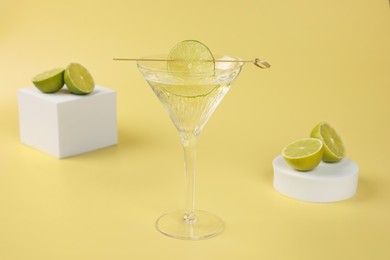 Martini cocktail with lime slice and fresh fruits on yellow background