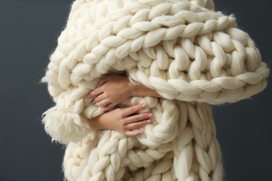 Photo of Woman holding soft knitted blanket on grey background, closeup