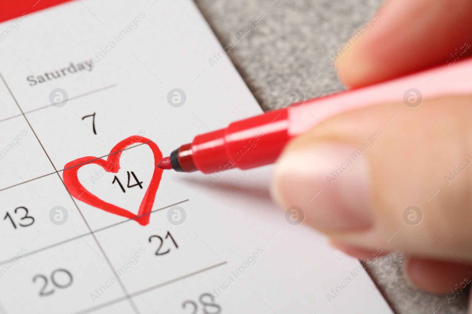 Photo of Woman marking Valentine's Day on calendar at grey table, closeup