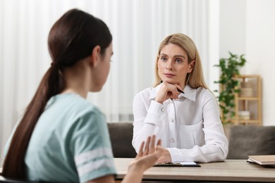 Psychologist working with teenage girl at table in office