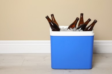 Photo of Blue plastic cool box with ice cubes and beer near beige wall indoors. Space for text