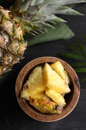Photo of Pieces of tasty ripe pineapple in bowl on dark wooden table, flat lay