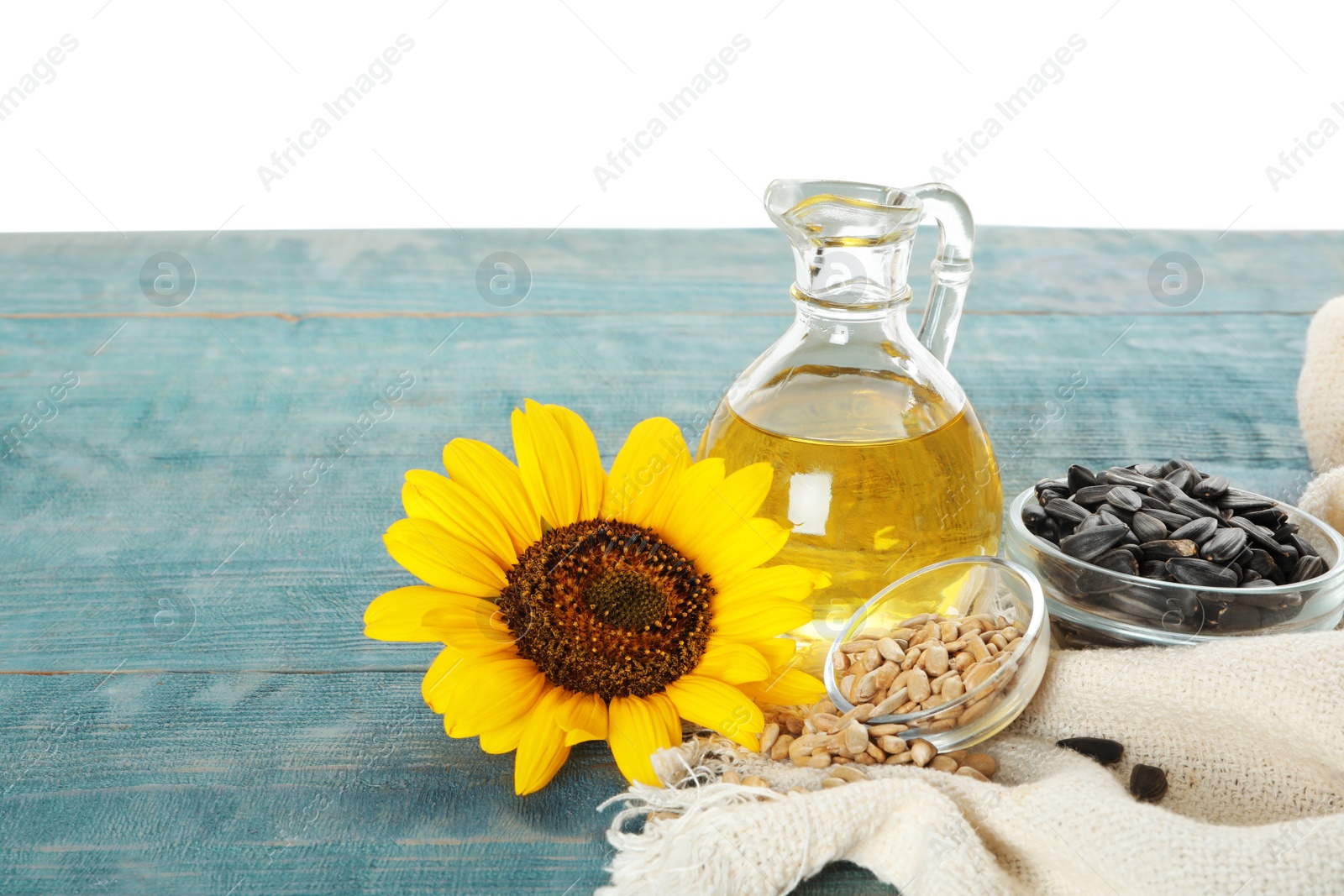 Photo of Sunflower, oil and seeds on light blue wooden table against white background