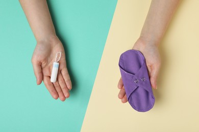 Photo of Woman holding reusable cloth menstrual pad and tampon on color background, top view
