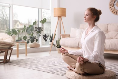 Photo of Woman meditating on wicker mat at home. Space for text