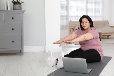 Photo of Overweight mature woman stretching while watching online class at home, space for text