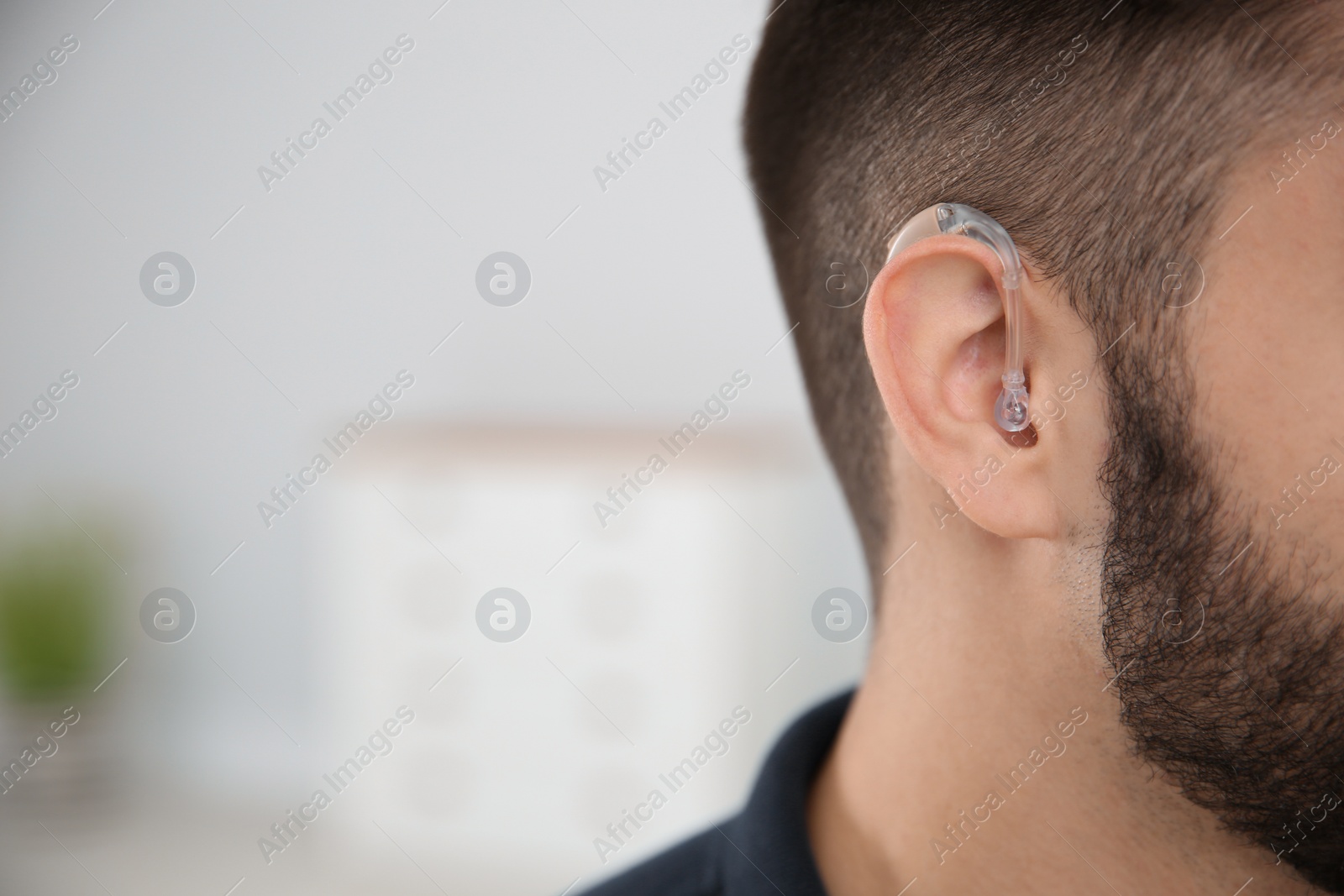 Photo of Young man with hearing aid indoors, closeup. Space for text