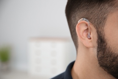 Young man with hearing aid indoors, closeup. Space for text