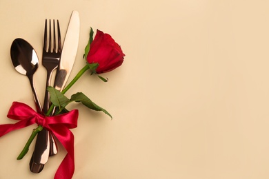 Beautiful cutlery set, flower and red bow on beige background, flat lay with space for text. Valentine's Day dinner