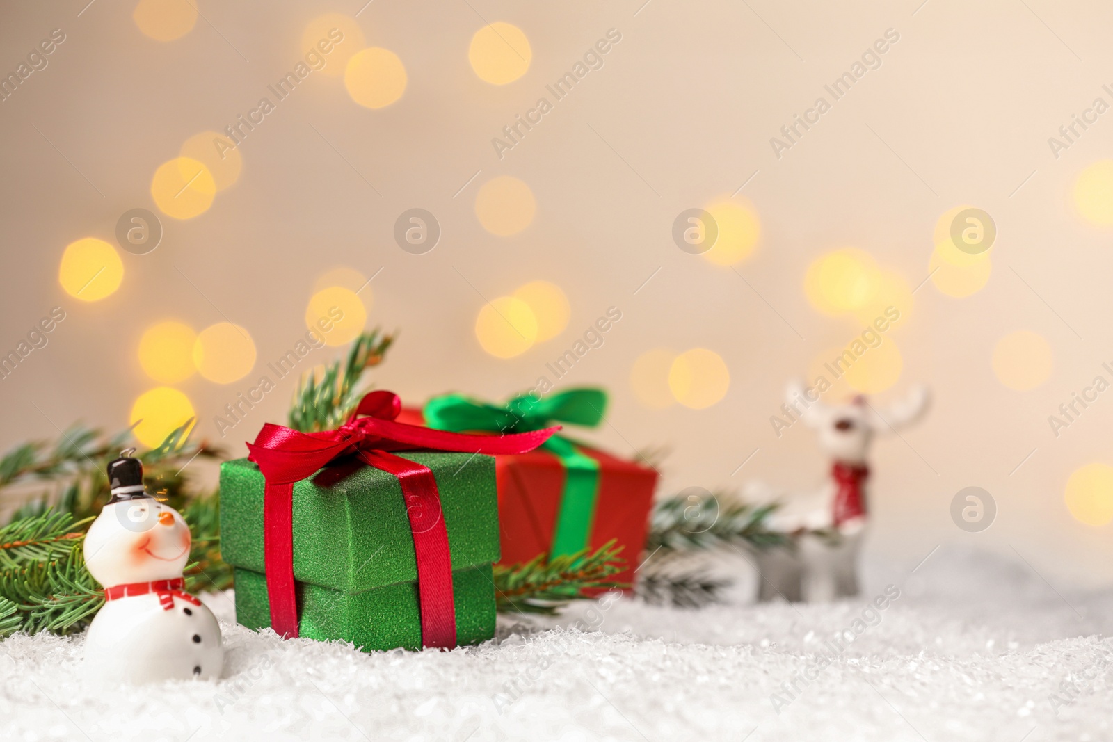 Photo of Gift boxes and Christmas decor on artificial snow against blurred festive lights, space for text