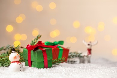 Photo of Gift boxes and Christmas decor on artificial snow against blurred festive lights, space for text