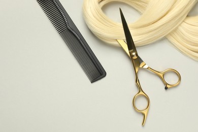 Professional hairdresser scissors and comb with blonde hair strand on light grey background, flat lay. Space for text