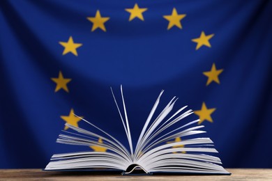 Photo of Open book on wooden table against flag of European Union