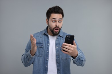 Emotional man using smartphone on grey background