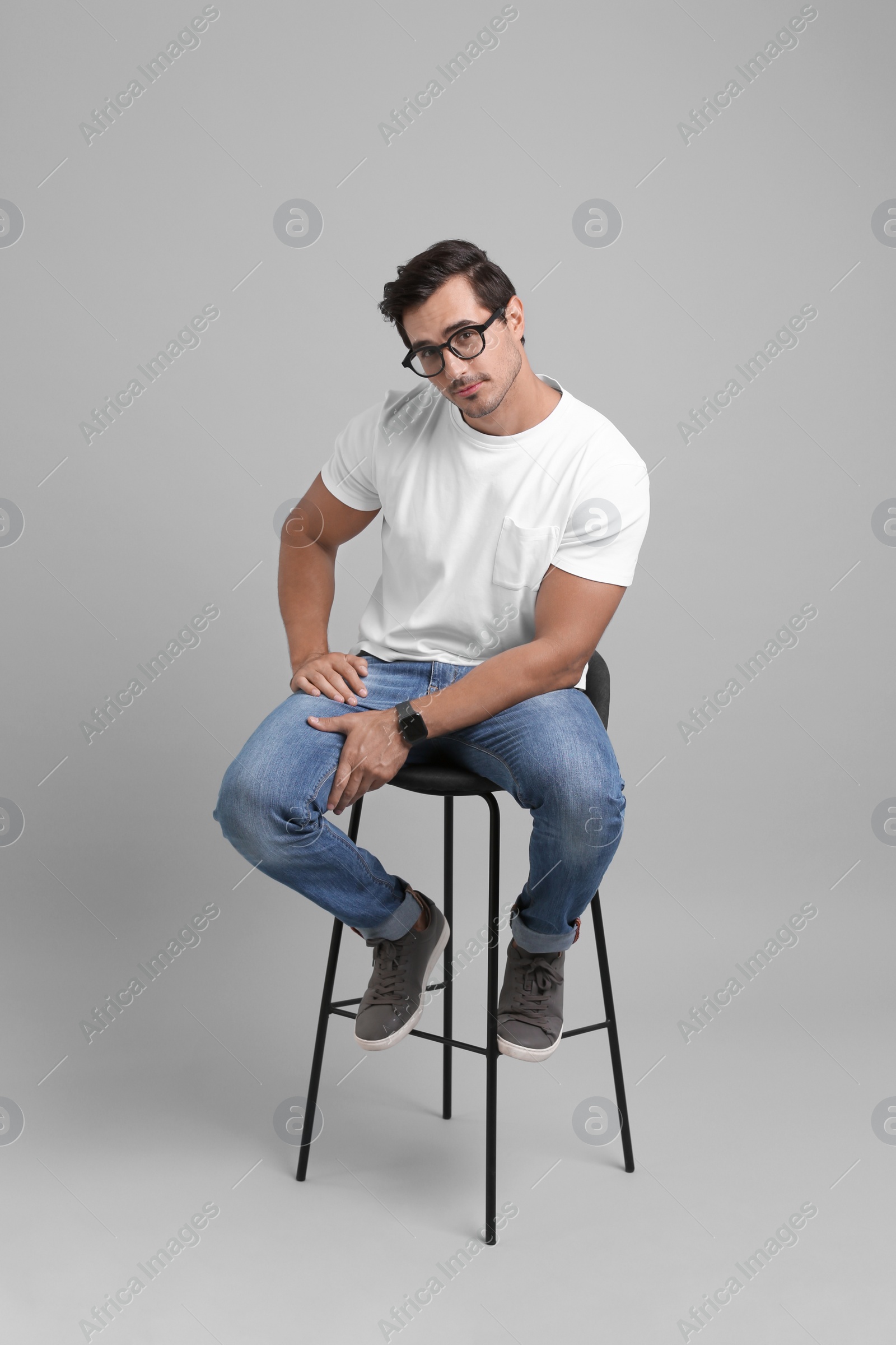 Photo of Handsome young man sitting on stool against grey background