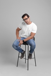 Photo of Handsome young man sitting on stool against grey background