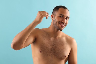 Photo of Handsome man applying cosmetic serum onto face on light blue background