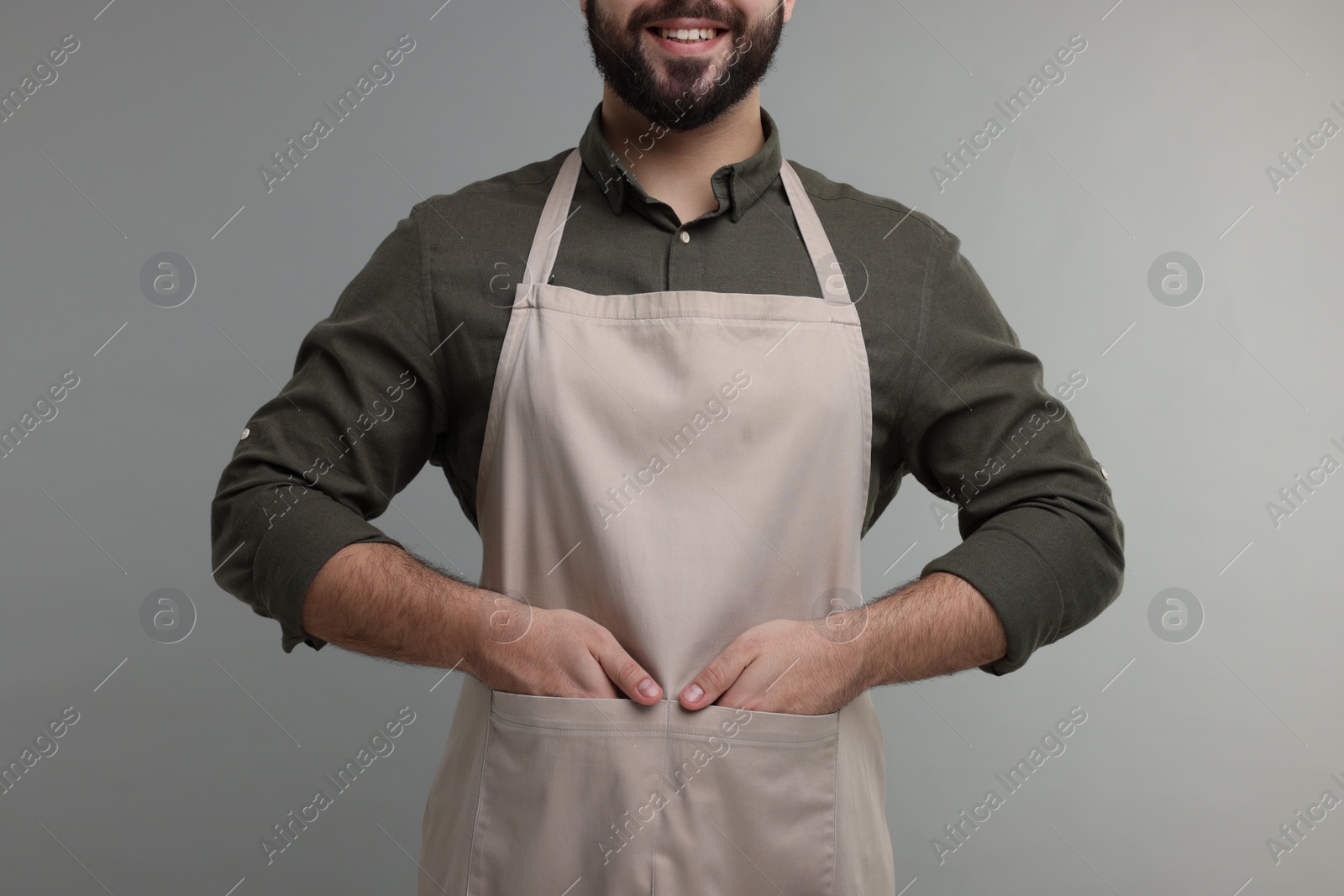 Photo of Smiling man in kitchen apron on grey background, closeup. Mockup for design