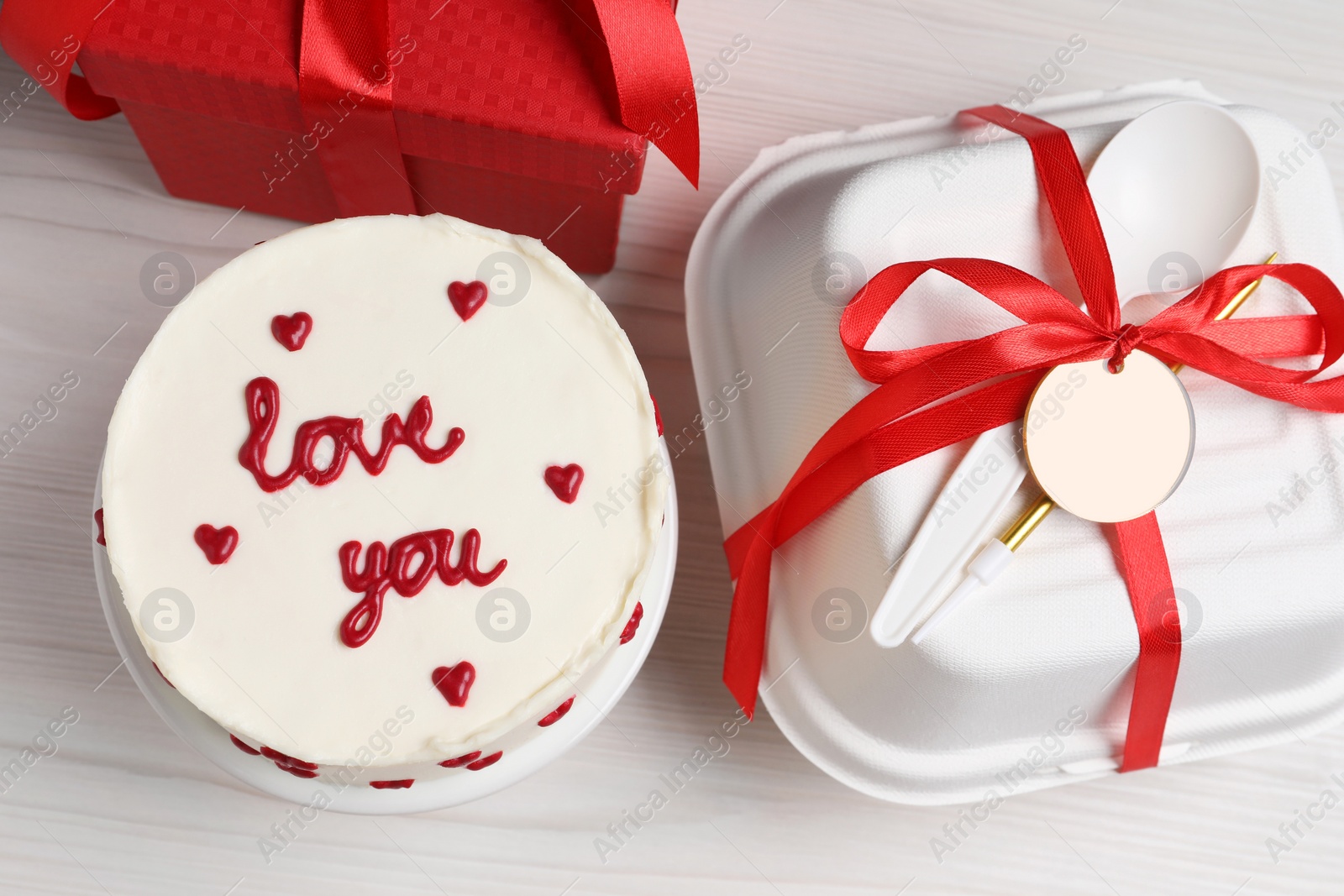 Photo of Bento cake with text Love You, gift box and takeaway packaging on white wooden table, flat lay. St. Valentine's day surprise