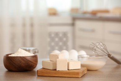 Pieces of compressed yeast and dough ingredients on wooden table indoors, space for text