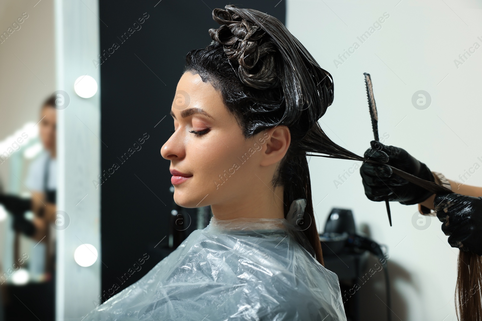 Photo of Professional hairdresser dyeing client's hair in beauty salon