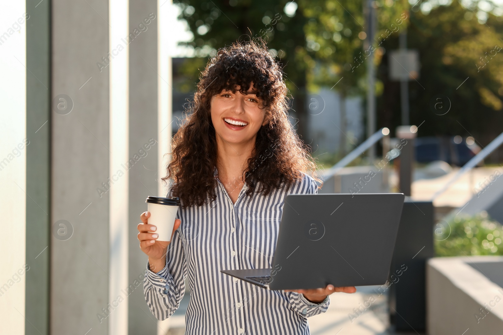 Photo of Happy young woman with cup of coffee using modern laptop outdoors