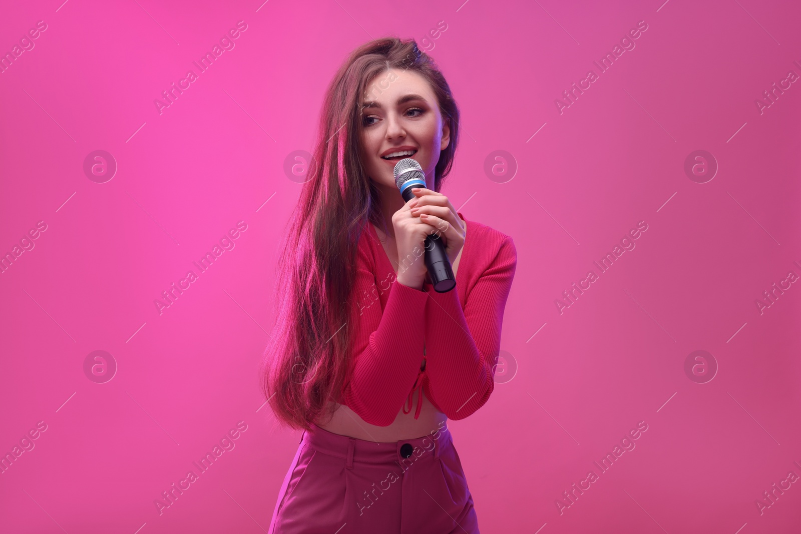 Photo of Emotional woman with microphone singing on pink background