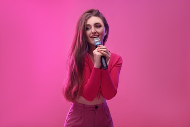 Emotional woman with microphone singing on pink background