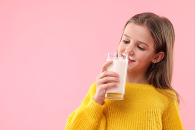 Photo of Cute little girl with milk mustache holding glass of tasty dairy drink on pink background. Space for text