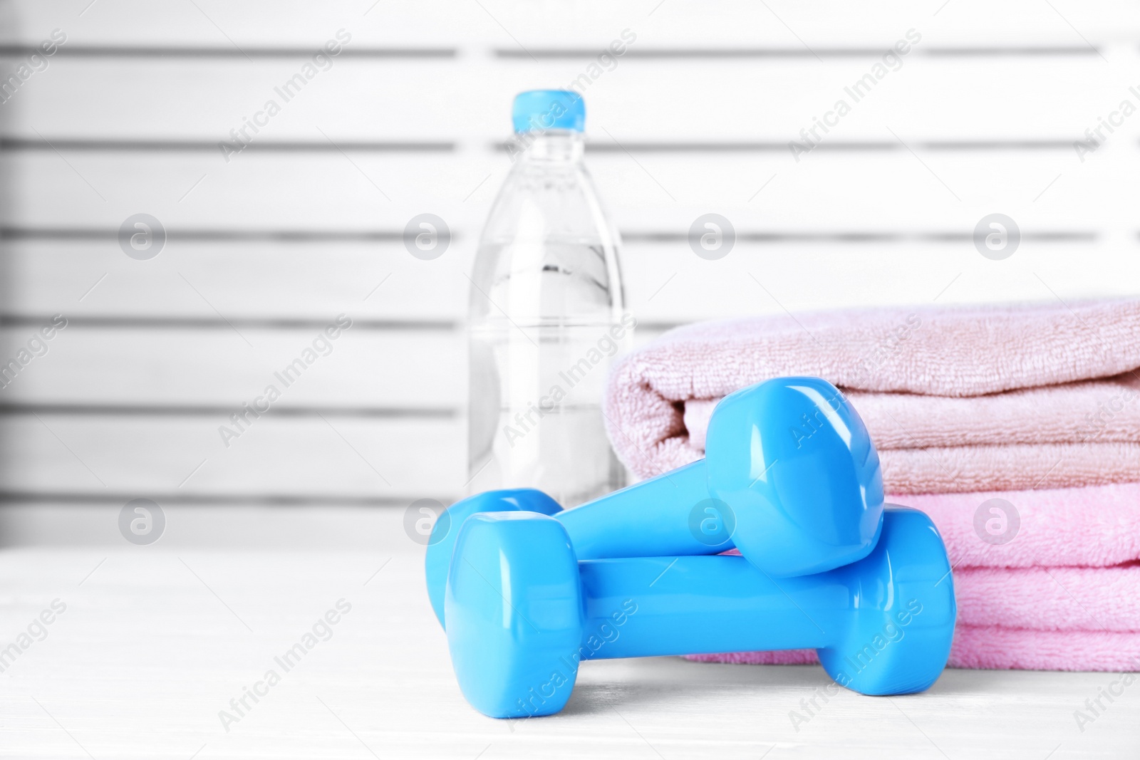 Photo of Vinyl dumbbells, bottle of water and towels on table, space for text