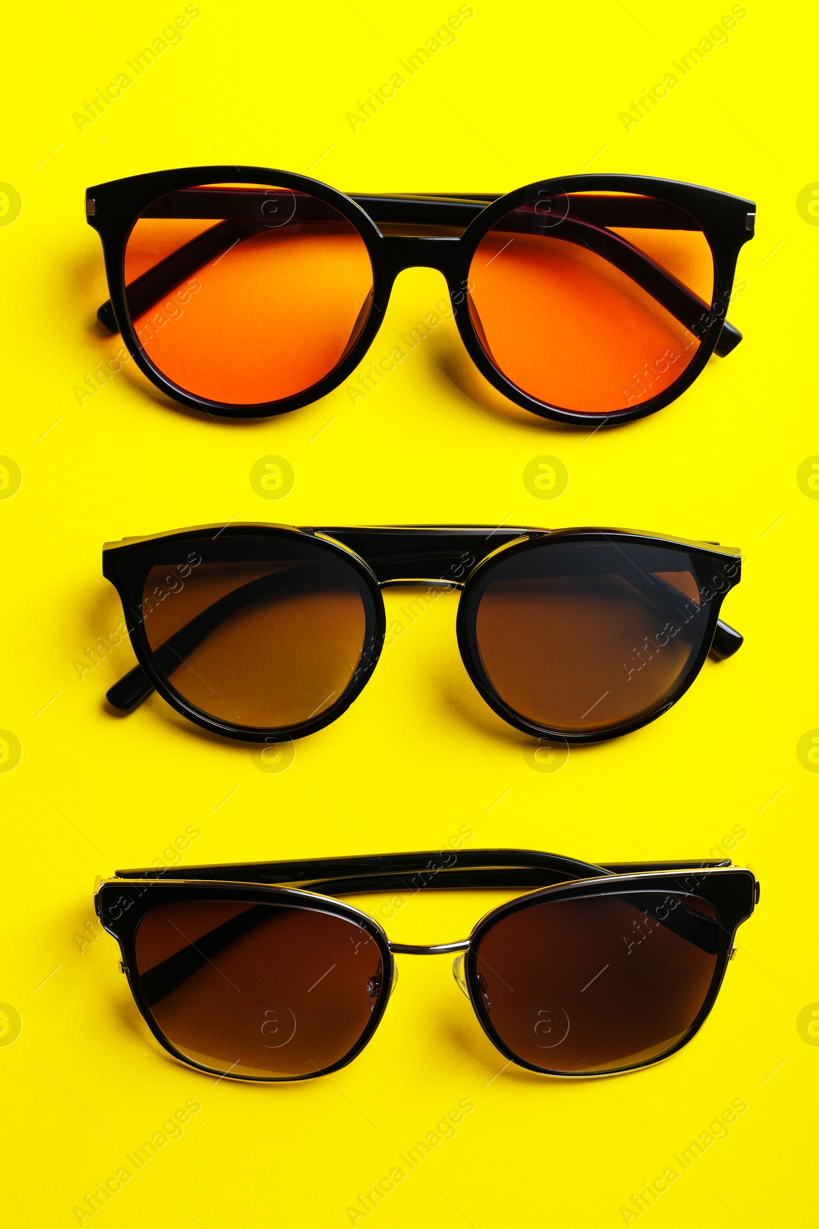 Photo of Many stylish sunglasses on yellow background, flat lay