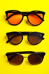 Photo of Many stylish sunglasses on yellow background, flat lay