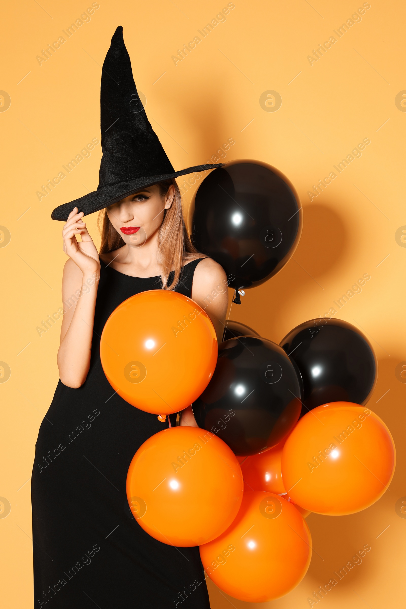 Photo of Beautiful woman wearing witch costume with balloons for Halloween party on yellow background