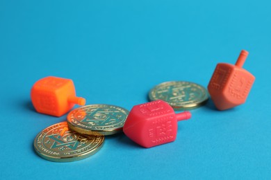 Dreidels with Jewish letters and coins on light blue background. Traditional Hanukkah game