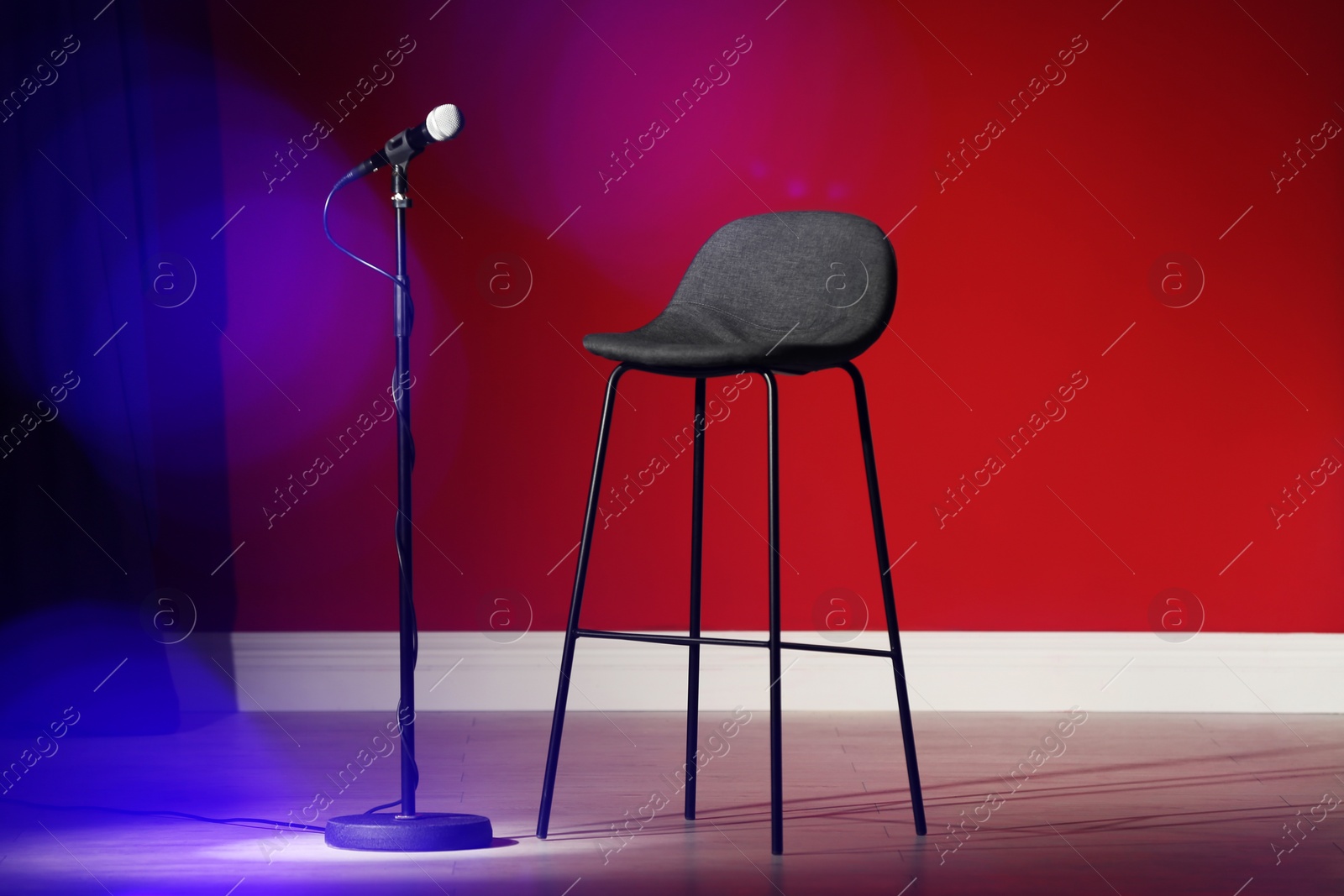 Photo of Microphone and stool on stage against color wall. Blurred lights