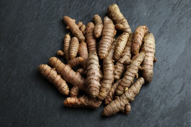 Photo of Many raw turmeric roots on black textured table, above view